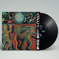 A vinyl record partially pulled from its sleeve, showing a colorful abstract cover artwork with stylized human figures and a black LP disc on a light gray background.