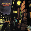 Album cover featuring a person in a costume standing on a street with neon signs and buildings.