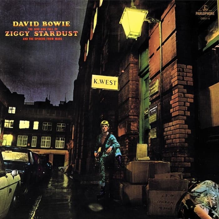 Album cover featuring a person in a costume standing on a street with neon signs and buildings.