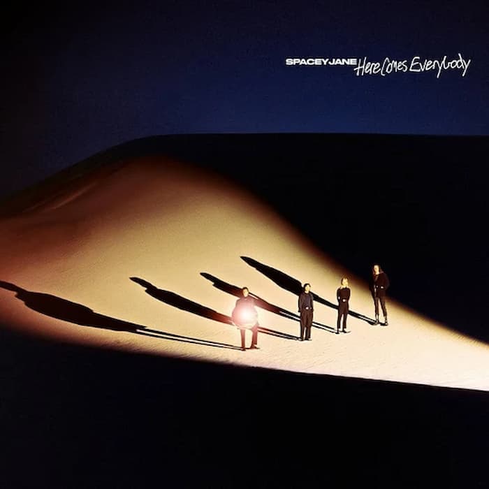 Album cover art for Spacey Jane's 'Here Lies Everybody', featuring three figures standing on a brightly lit sand dune under a dark blue sky, casting long shadows. The band's name and album title are printed in white at the top right.